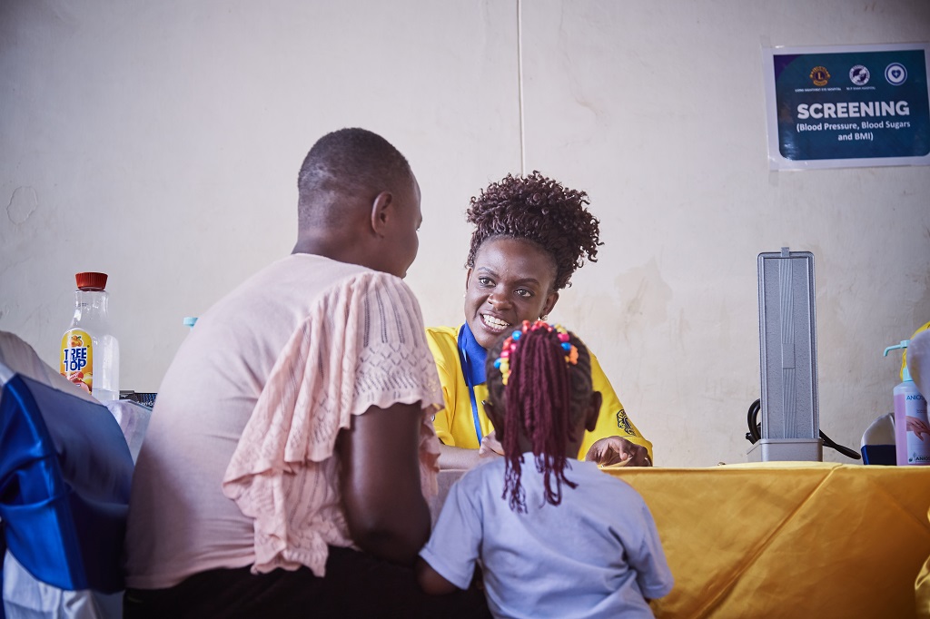 Kenyan Lion explains the diabetes screening to a mother and child